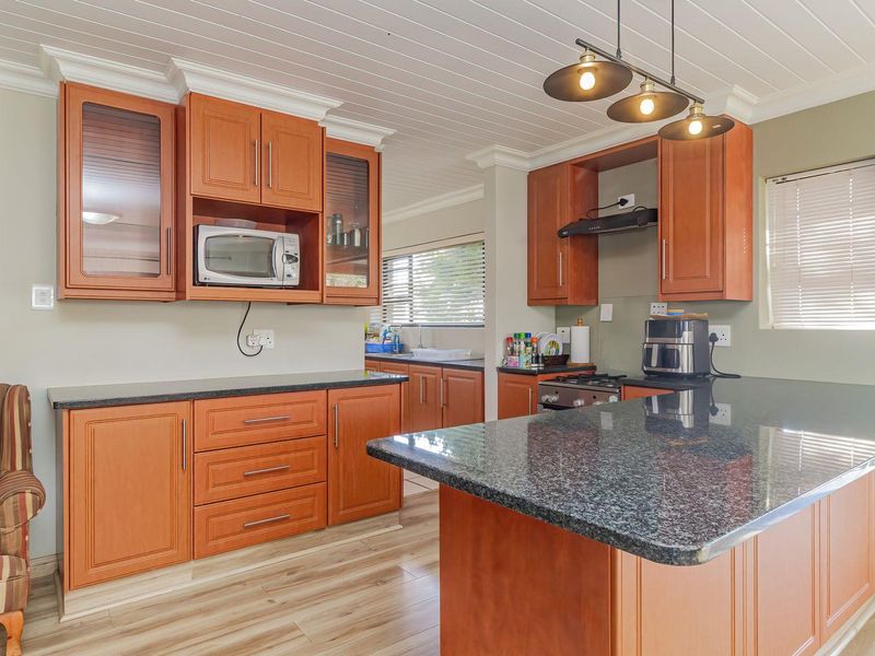 A functional kitchen featuring warm-toned wooden cabinetry, granite countertops, a gas hob with extractor, and a breakfast island, complemented by light laminate flooring.