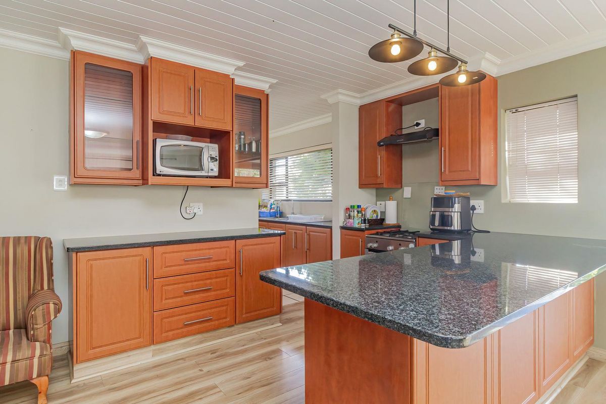 A functional kitchen featuring warm-toned wooden cabinetry, granite countertops, a gas hob with extractor, and a breakfast island, complemented by light laminate flooring.