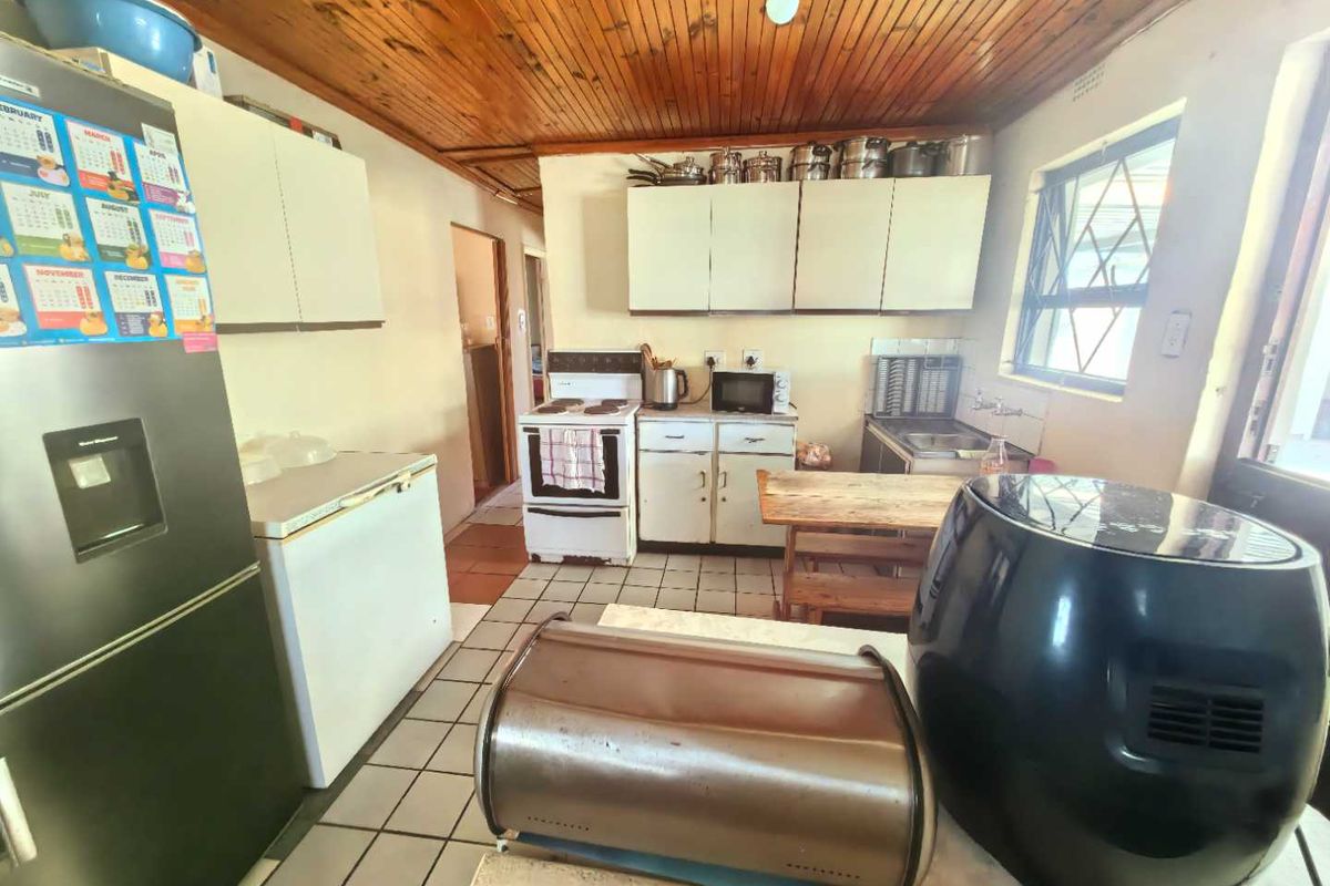 A dated kitchen featuring timber-clad ceilings, tiled flooring, and basic cabinetry with a freestanding stove and sink area.