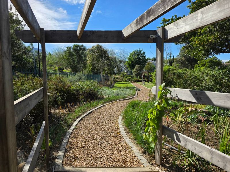 A well-maintained garden featuring a wooden pergola entrance leading to a gravel pathway bordered by stone edging and lush landscaping.
