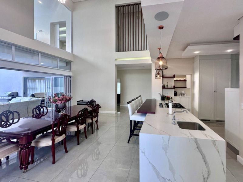 Spacious open-plan living and dining area featuring a modern kitchen with a stone-topped island, high ceilings, and seamless flow to the outdoor patio.
