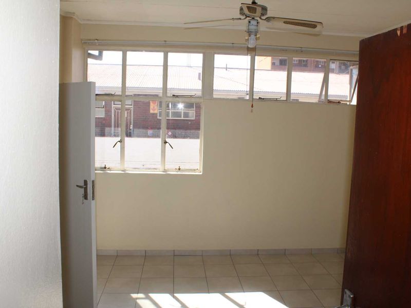 An empty bedroom featuring tiled flooring, a ceiling fan, and large casement windows allowing for natural light.