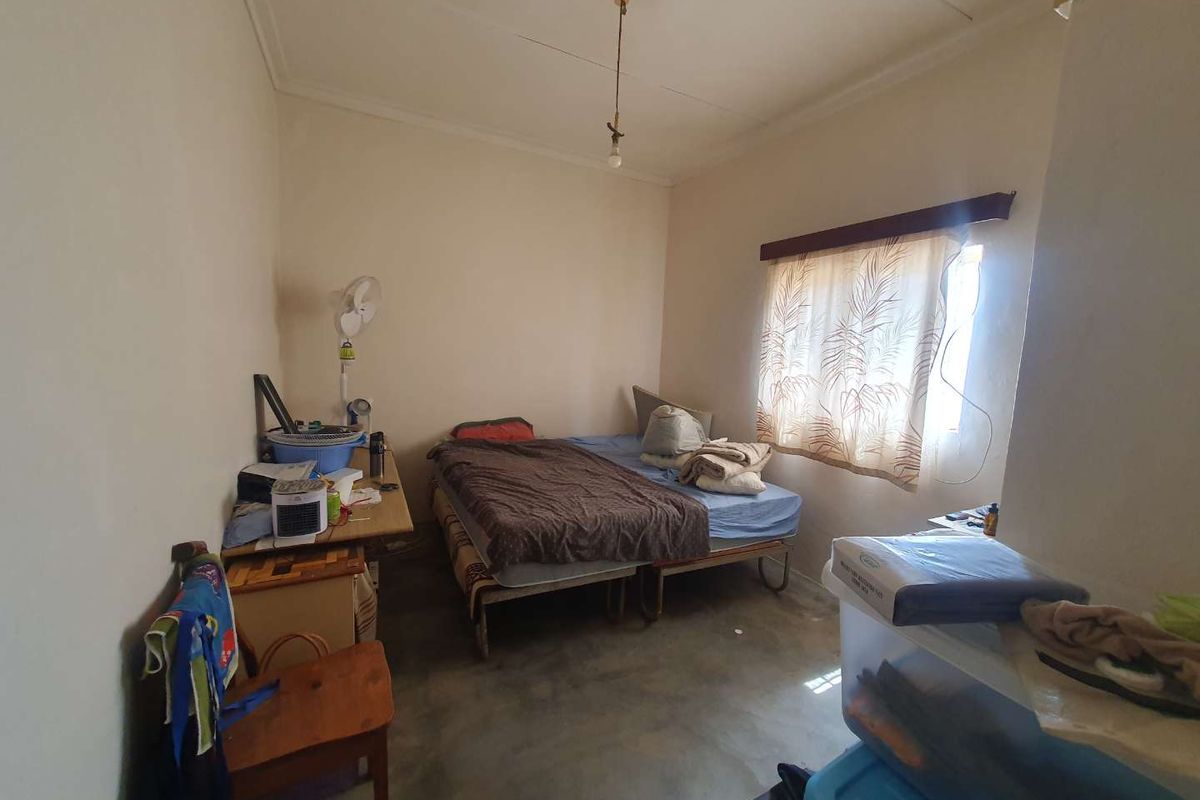 A simple bedroom featuring a window with a curtain rod and basic ceiling lighting, finished with a concrete floor.