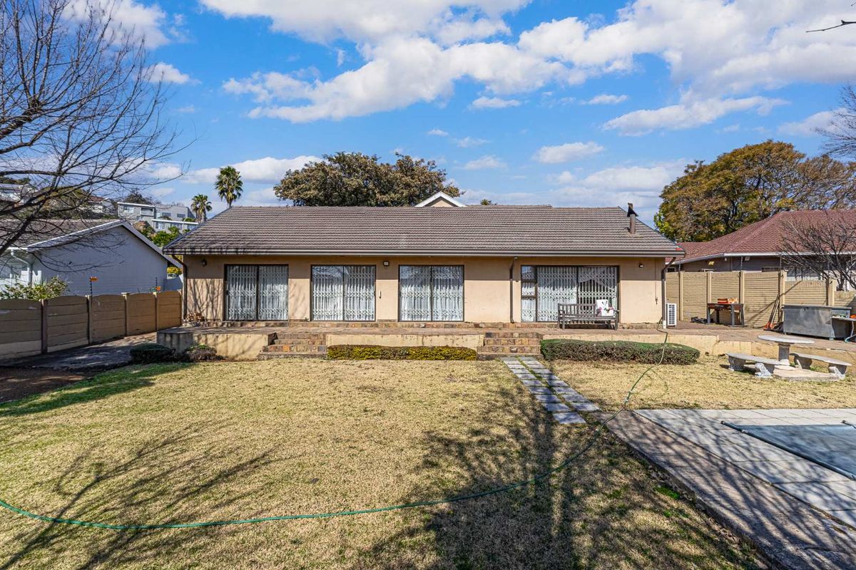 Rear view of the house featuring a tiled roof, multiple sliding glass doors, and a raised brick patio overlooking the garden.