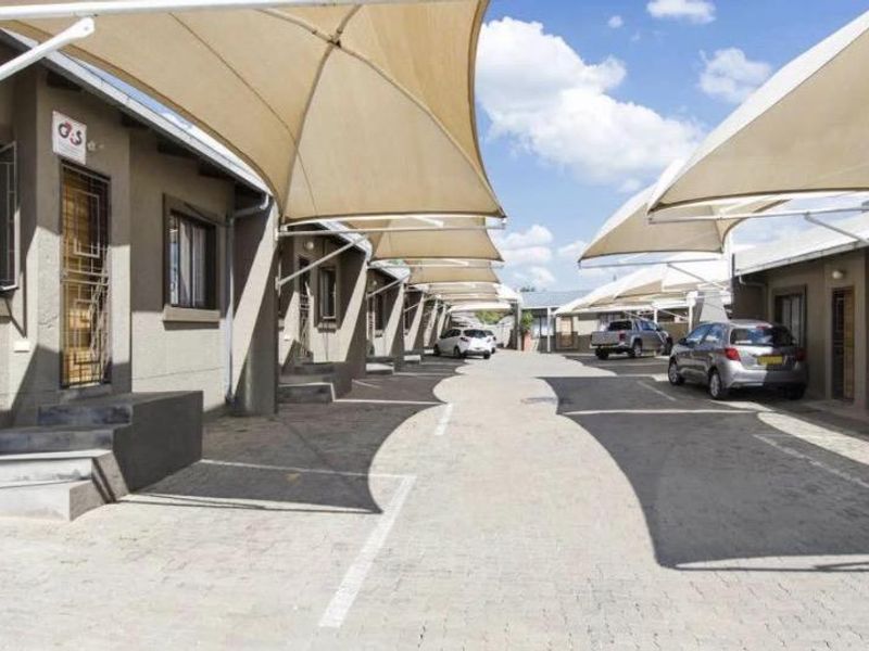 Exterior view of a townhouse complex featuring a paved driveway with multiple shade sail carports and secure unit entrances.