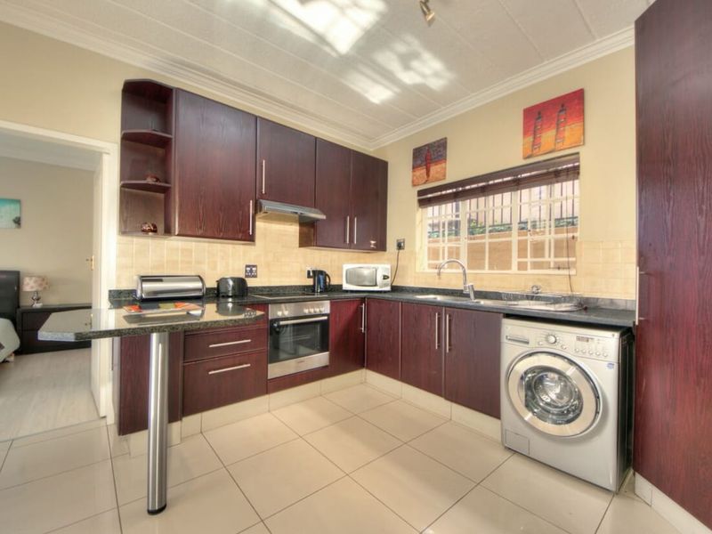 A functional kitchen featuring dark wood cabinetry, granite countertops, a built-in oven, and an integrated laundry space, with tiled flooring and a breakfast bar.