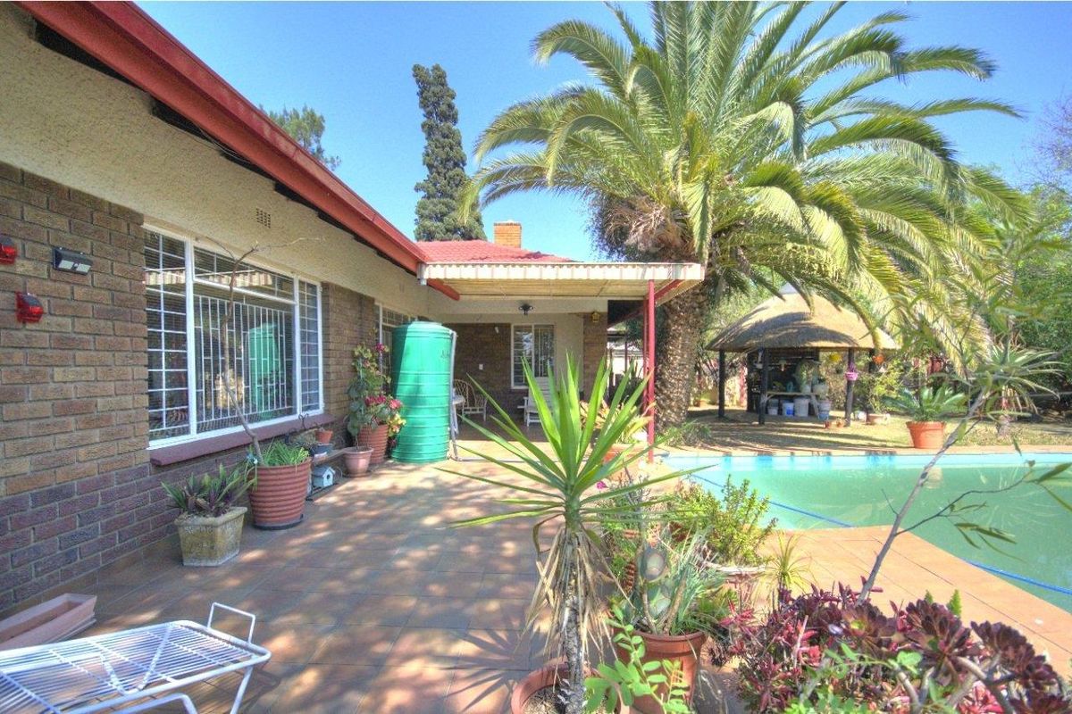 Rear exterior view featuring a covered patio, swimming pool, and a thatched lapa area set within a landscaped garden.