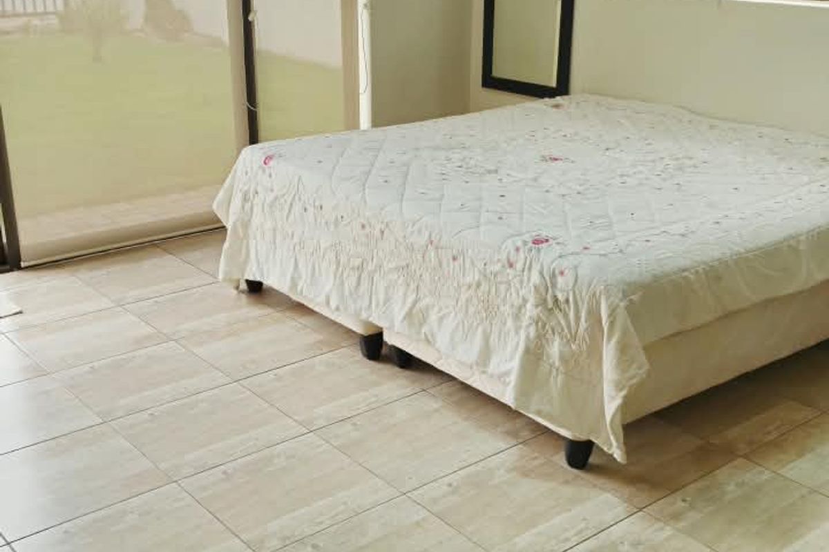 A bedroom featuring tiled flooring, large sliding glass doors providing outdoor access, and venetian blinds for light control.