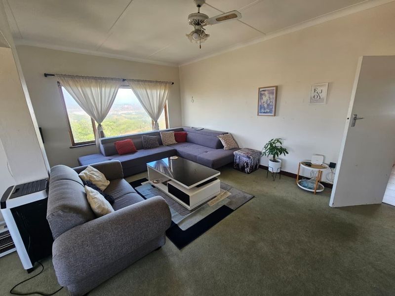 A living room featuring a ceiling fan, large window with scenic views, and carpeted flooring, offering a comfortable space with potential for modernization.