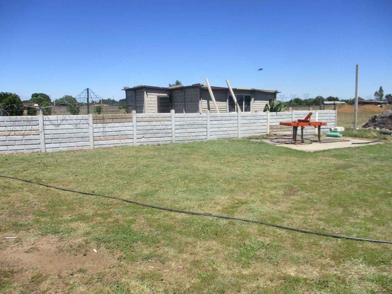 A view of the rear yard featuring a precast concrete boundary wall, barbed wire fencing, and an unfinished masonry structure on the property.