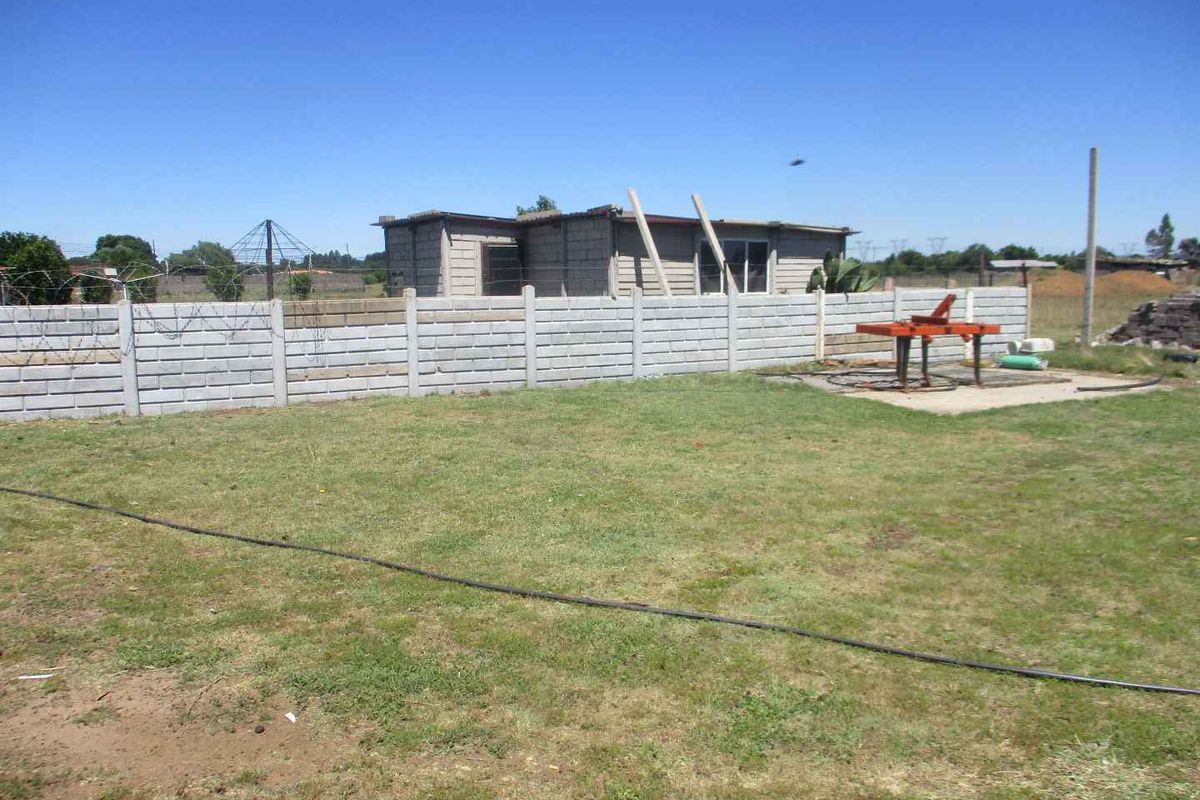 A view of the rear yard featuring a precast concrete boundary wall, barbed wire fencing, and an unfinished masonry structure on the property.