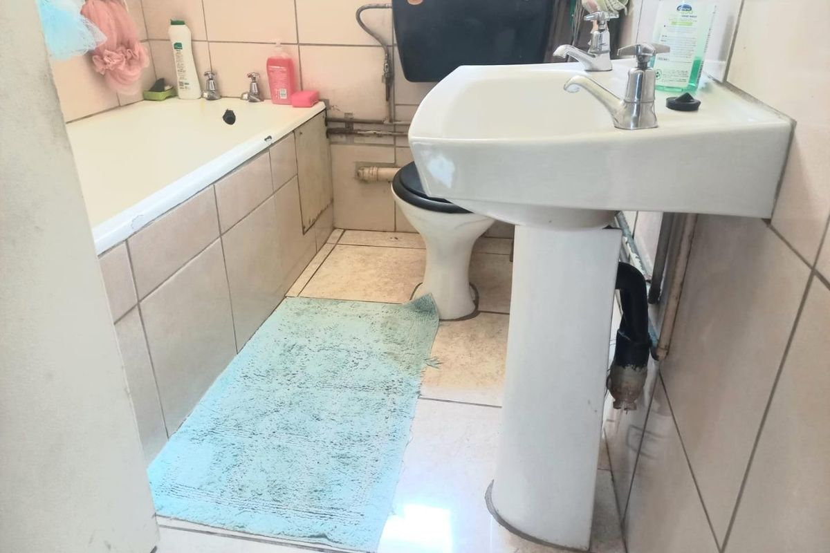 A dated bathroom featuring a pedestal sink, bathtub, and toilet with visible plumbing and ceramic tiling throughout.