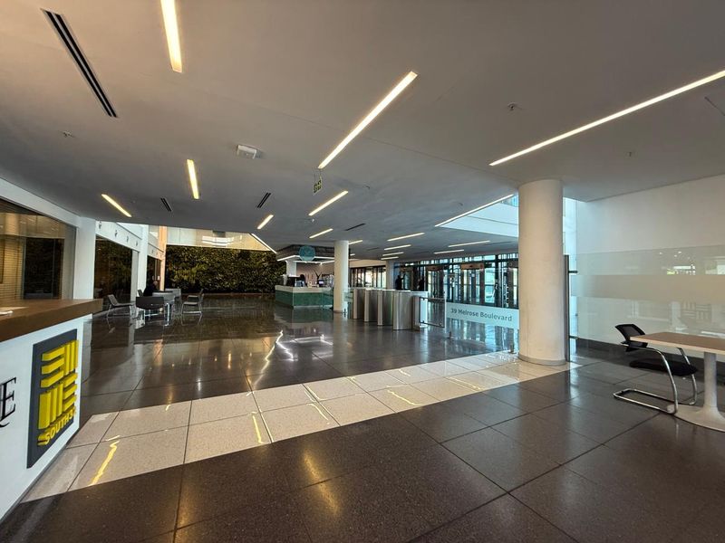 Spacious modern office building lobby featuring polished tile floors, recessed linear lighting, security turnstiles, and a prominent vertical garden wall.