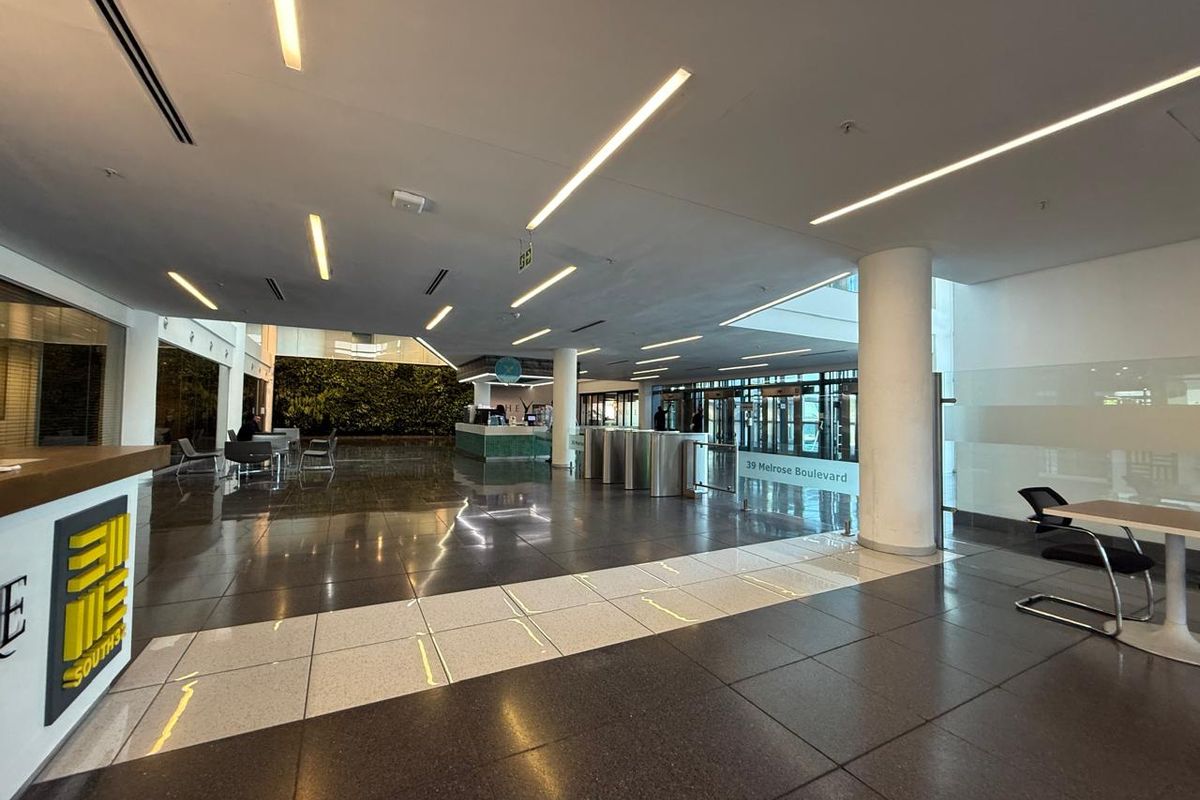 Spacious modern office building lobby featuring polished tile floors, recessed linear lighting, security turnstiles, and a prominent vertical garden wall.
