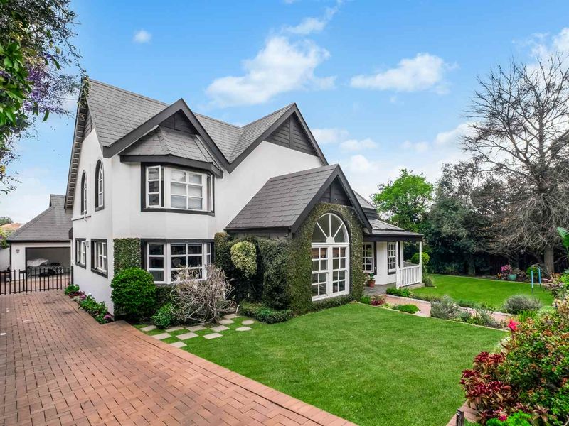 A charming two-story residence featuring a well-maintained garden, brick driveway, and distinctive architectural details including arched and bay windows.