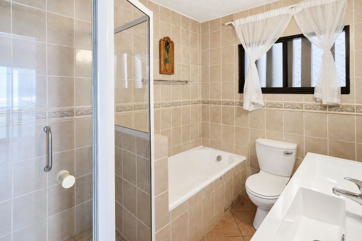 A functional bathroom featuring a built-in bathtub, separate shower enclosure, toilet, and vanity basin with neutral wall and floor tiling.