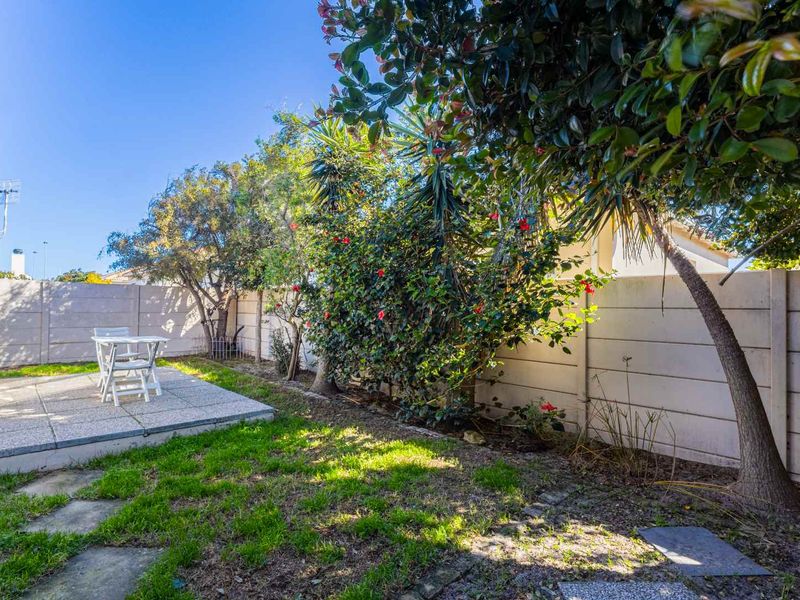 A private rear garden featuring a paved patio area, established trees, and a secure precast concrete boundary wall.