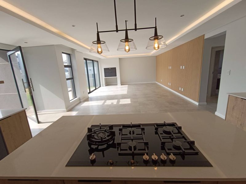 Spacious open-plan living area featuring a modern kitchen island with gas hob, timber slat feature wall, built-in fireplace, and large sliding doors to outside.