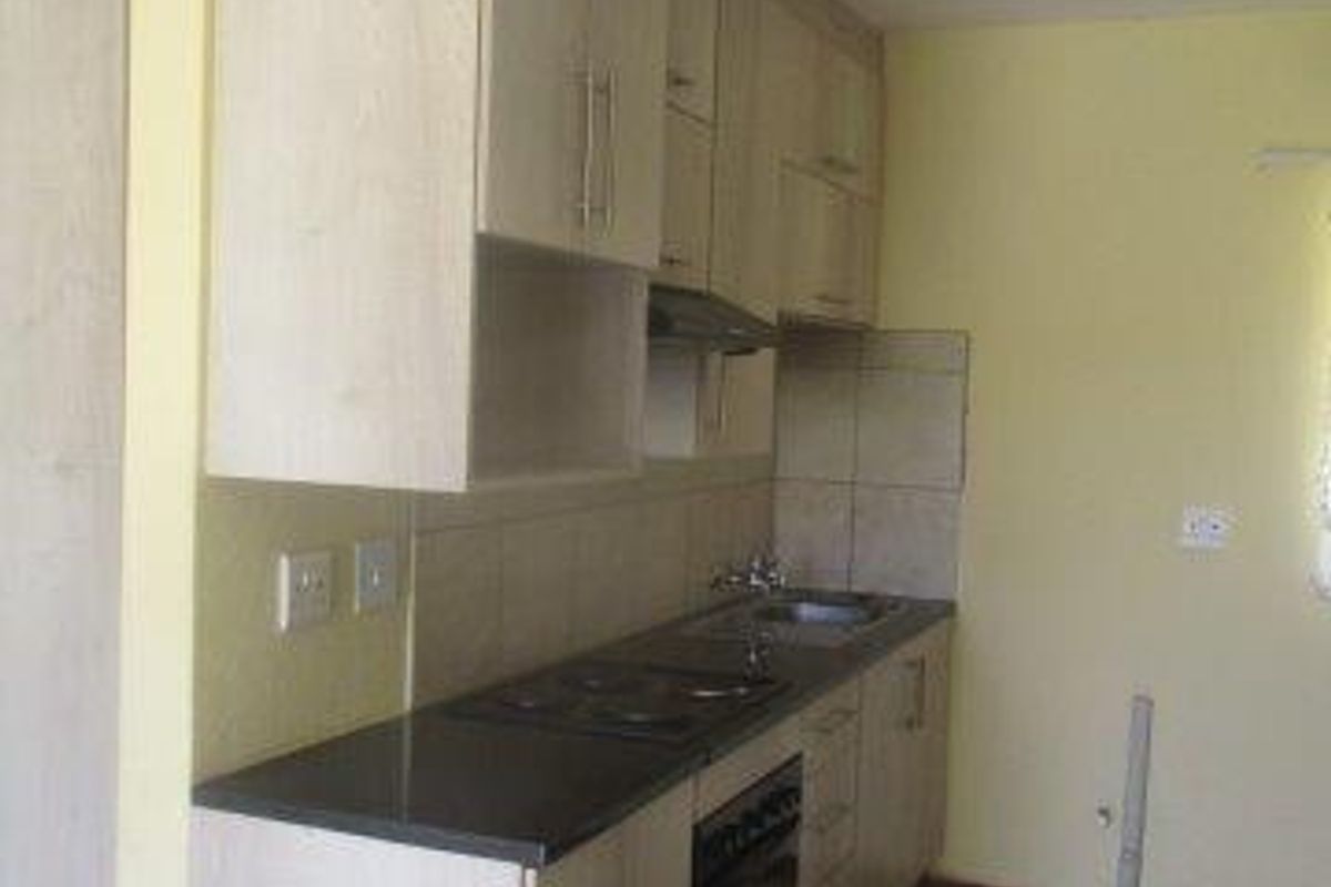 A functional kitchen featuring light wood-finish cabinetry, dark countertops, integrated oven and hob, and tiled flooring in a neutral, well-maintained space.