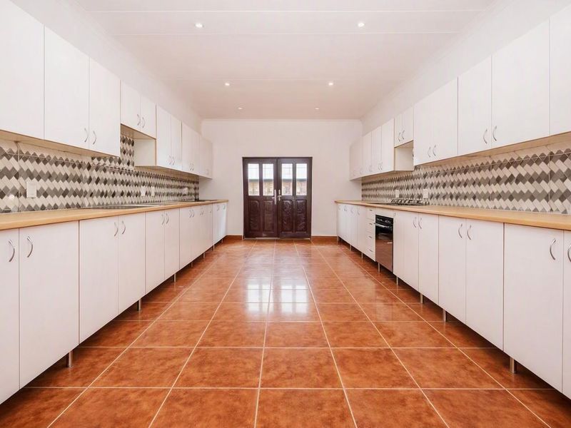 Spacious galley-style kitchen featuring extensive white cabinetry, laminate countertops, a decorative tiled backsplash, and durable ceramic floor tiles.