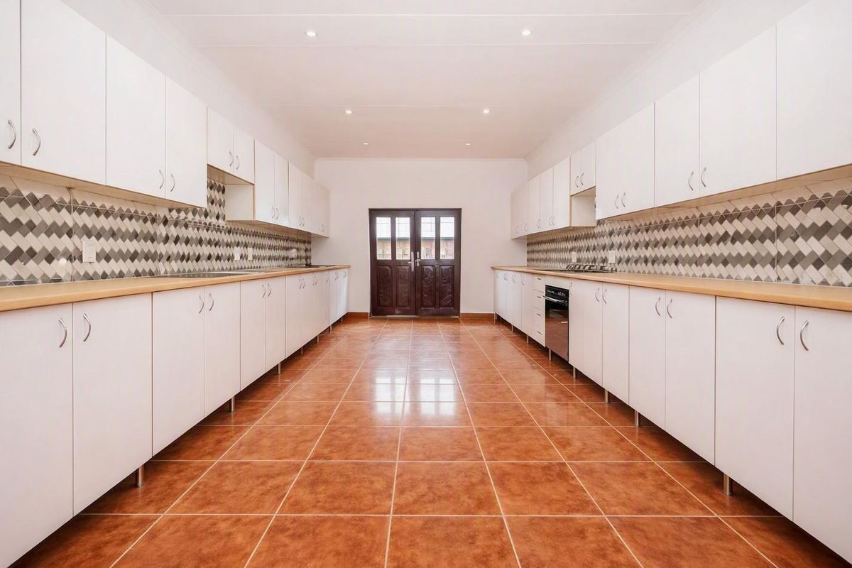 Spacious galley-style kitchen featuring extensive white cabinetry, laminate countertops, a decorative tiled backsplash, and durable ceramic floor tiles.