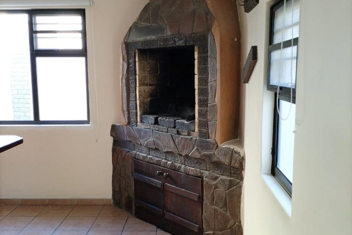 A living area featuring a corner stone-clad fireplace, tiled flooring, and exposed ceiling beams, providing a rustic focal point for the room.