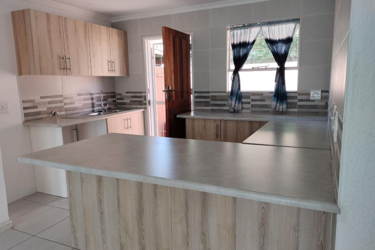 A functional kitchen featuring light wood-look cabinetry, neutral tiled splashbacks, a breakfast nook, and direct access to the exterior.