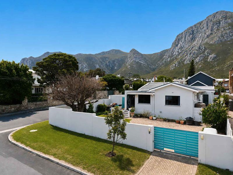 Front exterior view of a well-maintained house featuring a paved driveway, secure boundary wall with a sliding gate, and scenic mountain backdrop.