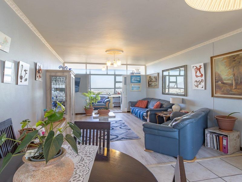 Spacious open-plan living and dining area featuring laminate and tiled flooring, crown molding, and large windows providing natural light and views.