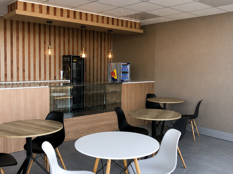 A modern retail or cafe space featuring a built-in service counter, wooden slat wall accents, suspended ceiling, and durable tiled flooring.