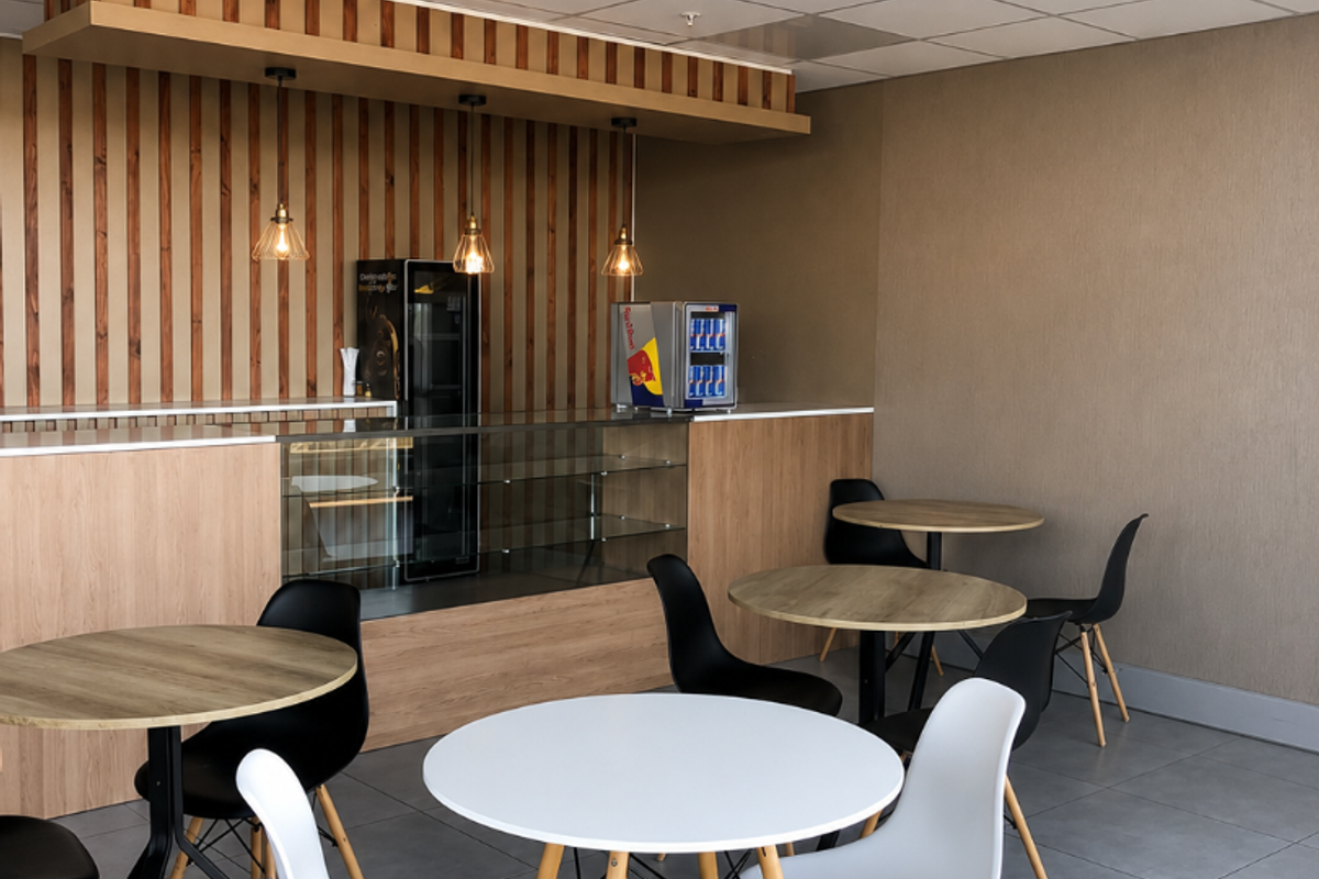A modern retail or cafe space featuring a built-in service counter, wooden slat wall accents, suspended ceiling, and durable tiled flooring.