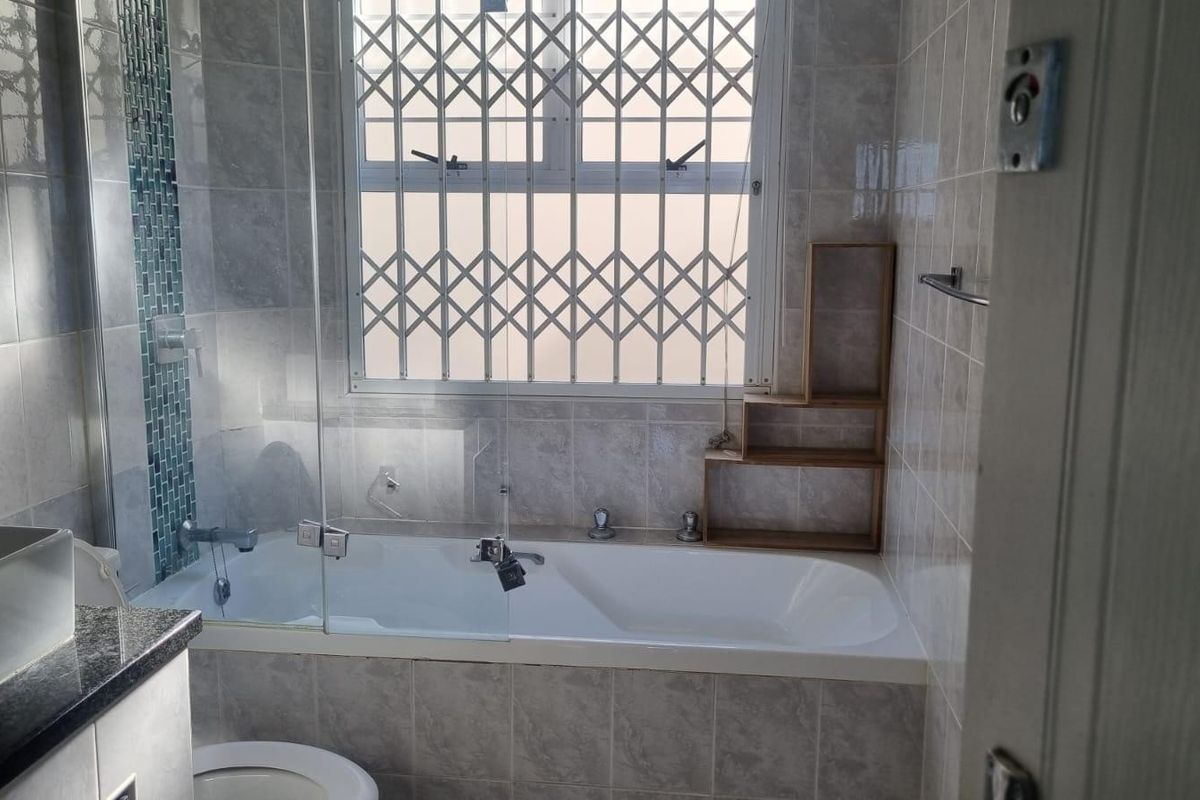 A well-maintained bathroom featuring a bathtub with a glass screen, tiled walls, and a secure window with a metal security gate.