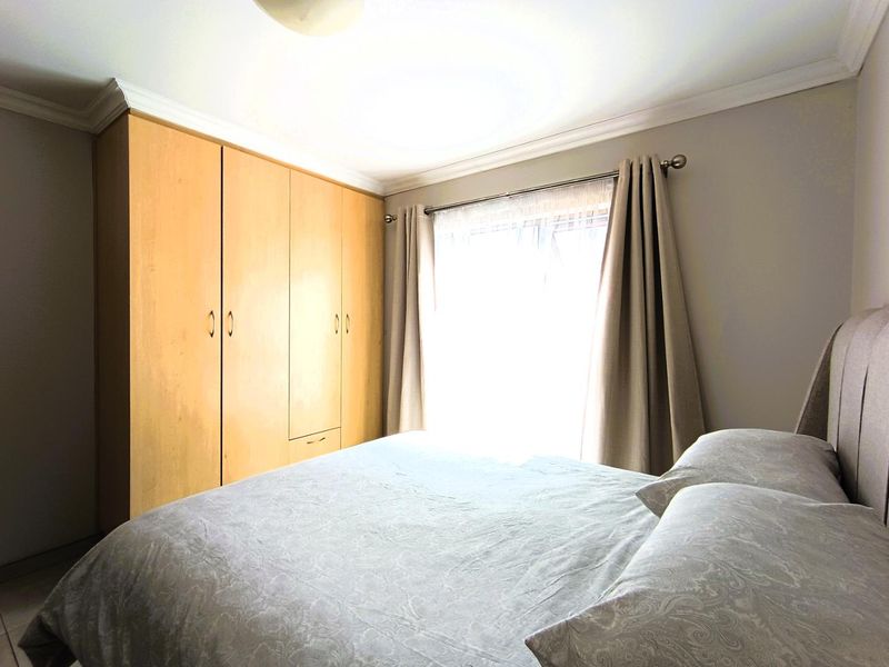 A bedroom featuring built-in wooden cupboards, neutral wall finishes, and natural light from the window.