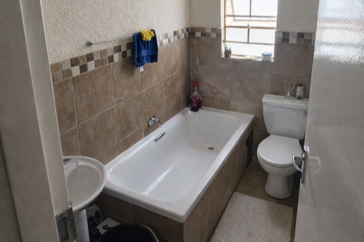 A compact bathroom featuring a built-in bathtub, pedestal basin, and toilet with neutral wall tiling and a window for natural light.