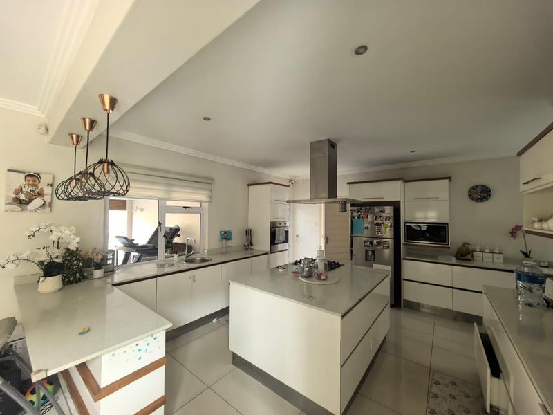 Modern kitchen featuring a central island, stone countertops, built-in appliances, and sleek cabinetry with recessed lighting and tiled floors.