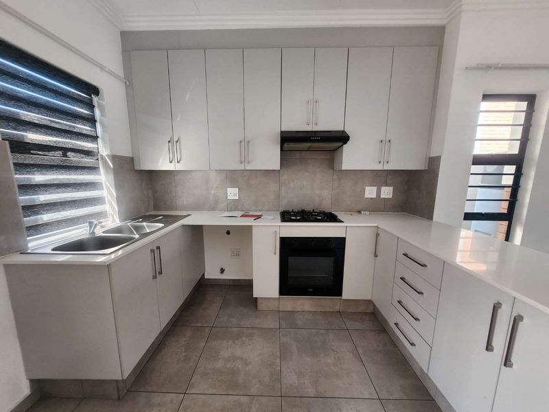 Modern kitchen featuring light grey cabinetry, stone countertops, built-in gas hob, oven, extractor fan, and double sink with tiled flooring.