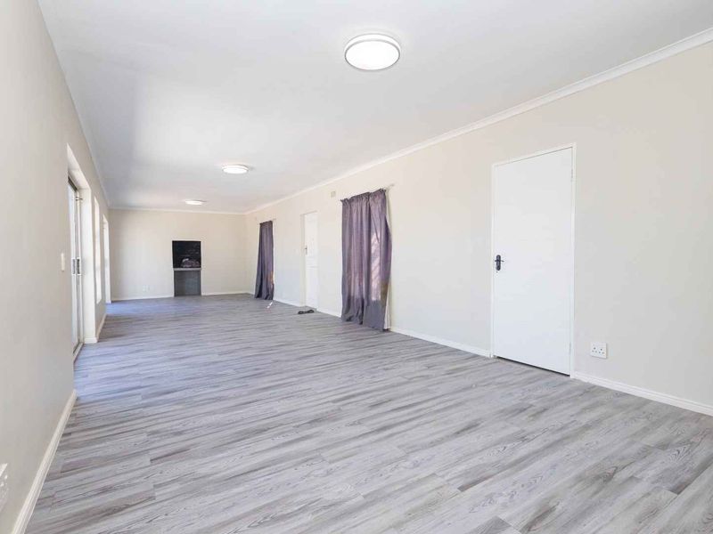 Spacious, empty living area featuring modern grey-toned laminate flooring, neutral walls, and sliding glass doors providing natural light.