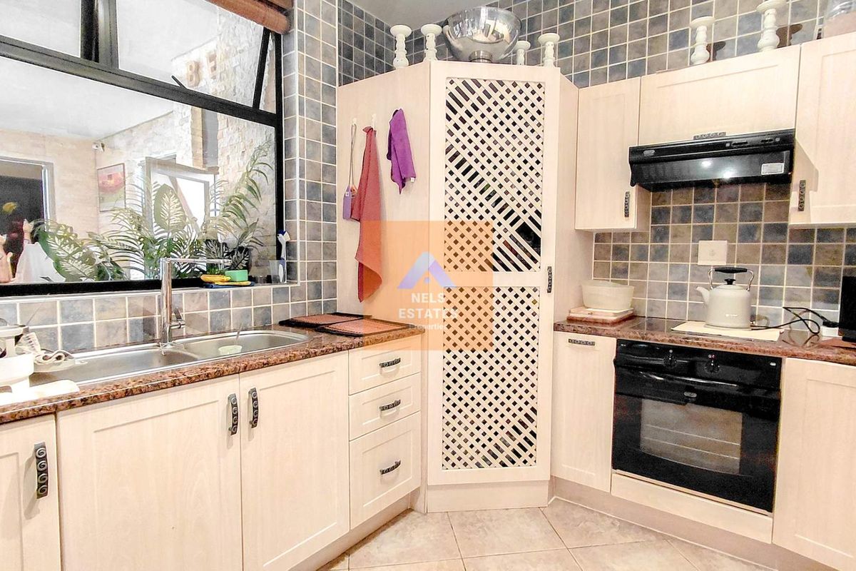 A functional kitchen featuring light-toned cabinetry, granite countertops, a built-in oven with extractor fan, and a double-basin sink with tiled splashbacks.
