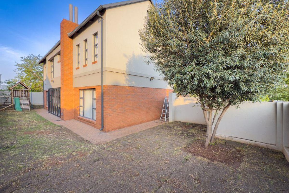 Rear view of the property featuring a brick and plaster facade, paved walkway, and a private garden area with established trees.