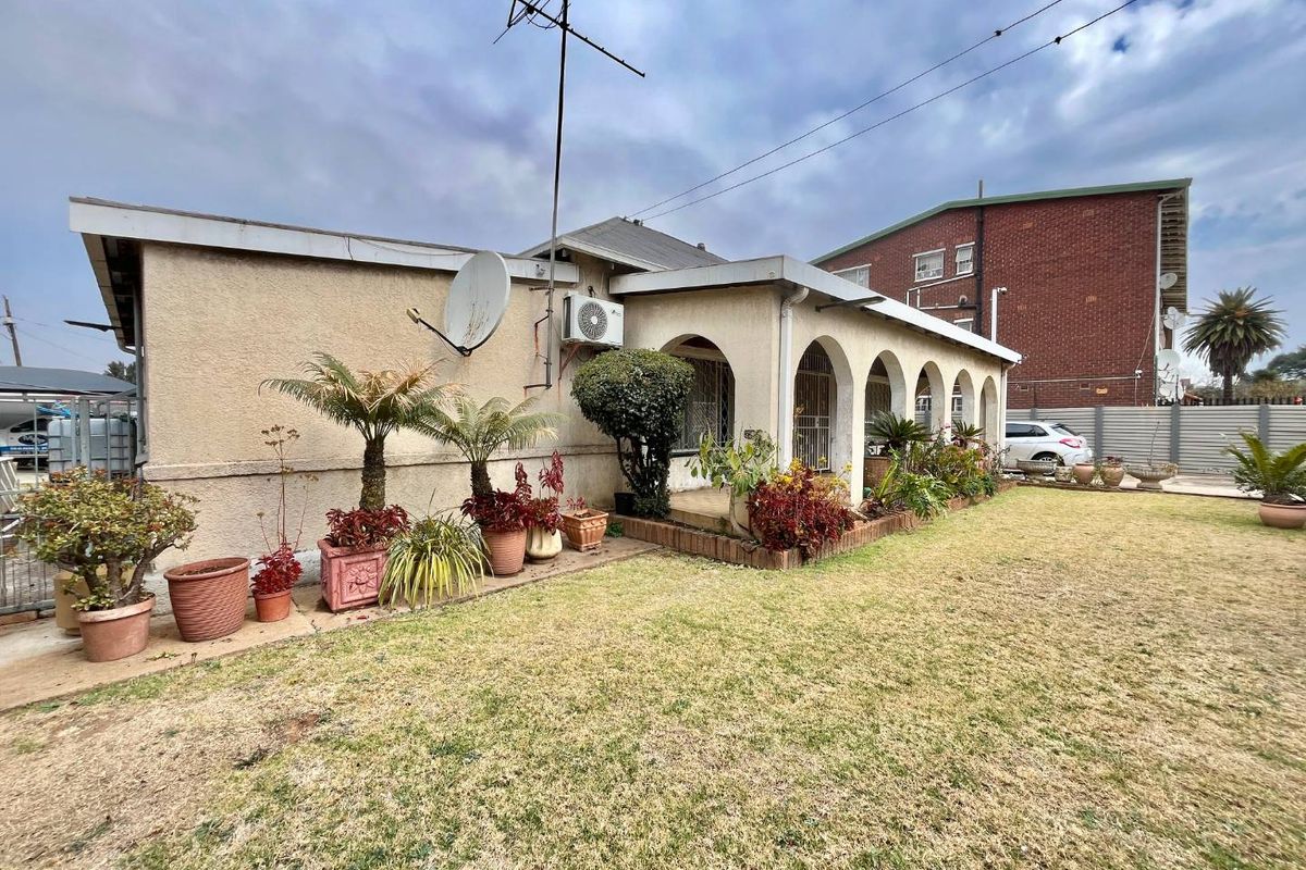 Rear view of the property featuring a covered patio with arched architectural details, a lawn area, and exterior wall-mounted air conditioning unit.