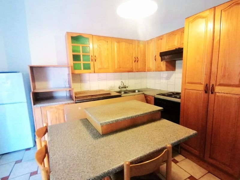 A functional kitchen featuring wooden cabinetry, laminate countertops, a double basin sink, and a tiled backsplash, offering a classic layout with ample storage space.