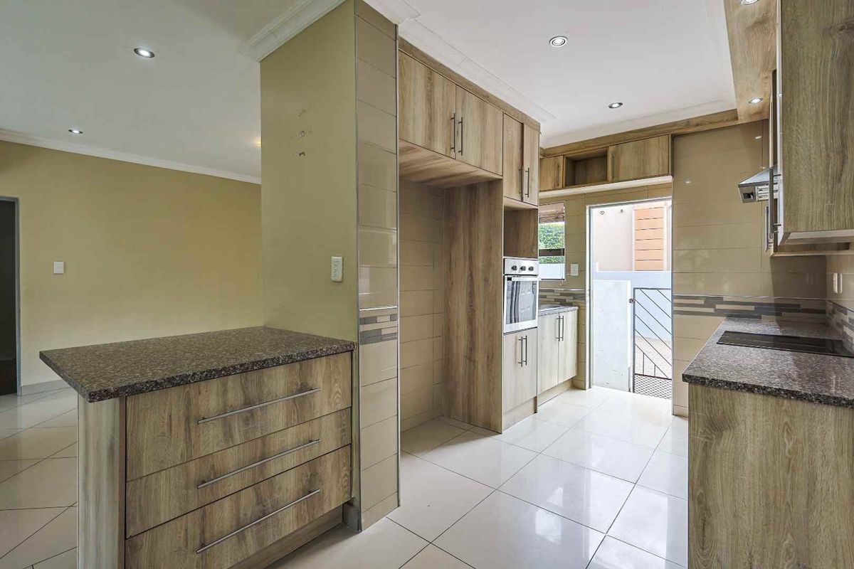 Modern kitchen featuring wood-look cabinetry, granite countertops, built-in oven, and tiled flooring, offering a clean and functional workspace.