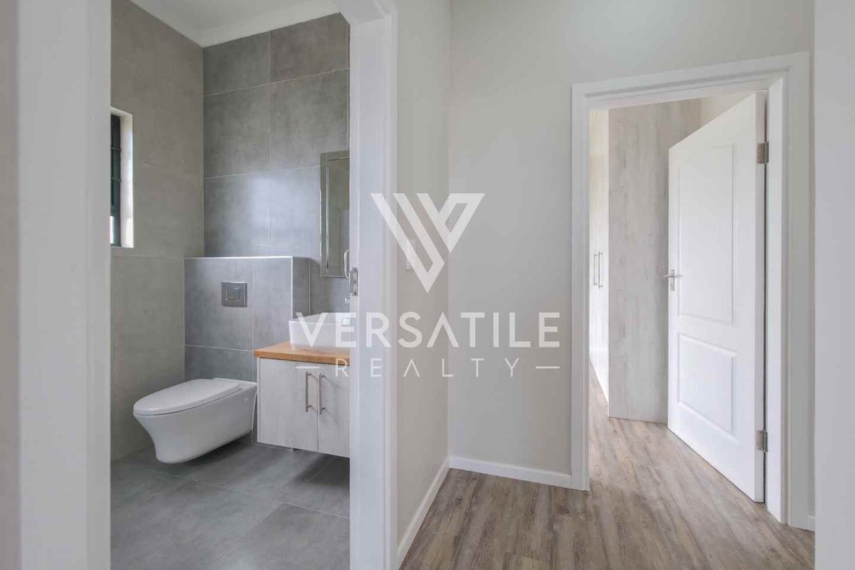 A modern, minimalist bathroom featuring a wall-hung toilet, timber-topped vanity, and neutral grey floor-to-ceiling tiling.