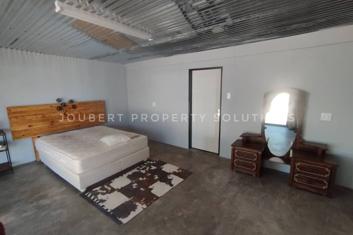 A spacious bedroom featuring a corrugated metal ceiling, concrete flooring, and neutral wall finishes, offering a functional and simple living space.