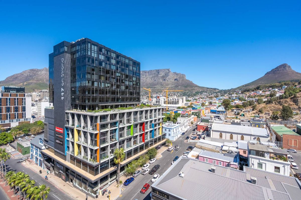 Aerial view of the 117 on Strand apartment building, showcasing its modern glass and concrete architecture against a mountain backdrop.