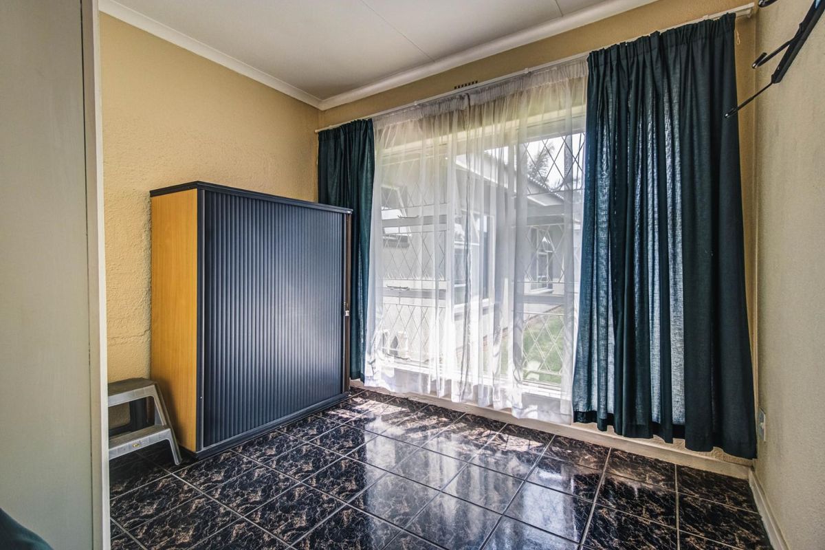 A bright, empty bedroom featuring dark tiled flooring, large windows with security bars, and neutral wall finishes.