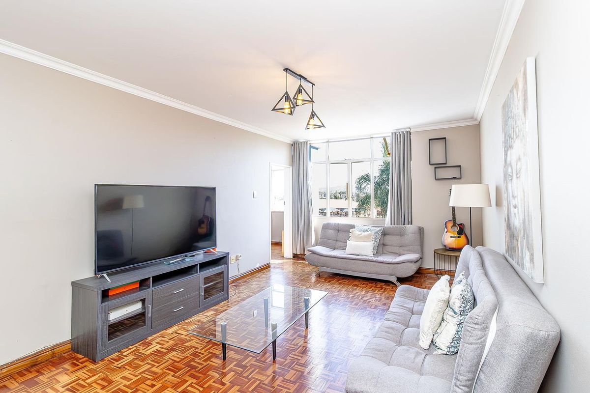 A bright living room featuring classic parquet flooring, crown molding, and a large window providing natural light.