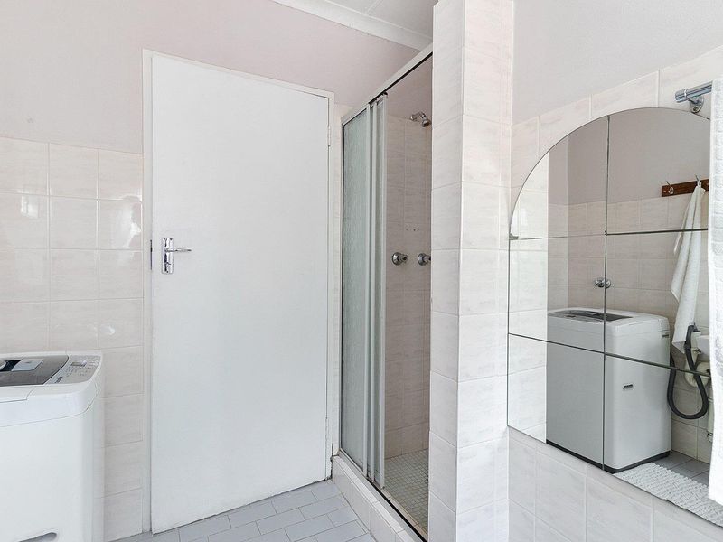 A functional laundry area featuring tiled walls, a built-in shower enclosure, and a large wall-mounted mirror.