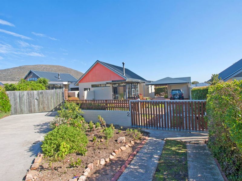 Front view of a detached house featuring a concrete driveway, timber fencing, carport, and a modern metal roof design.