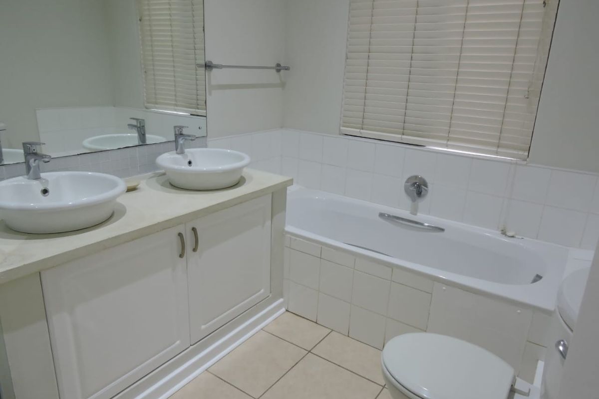 A clean, functional bathroom featuring a double vanity with vessel sinks, a built-in bathtub, tiled flooring, and neutral finishes throughout.